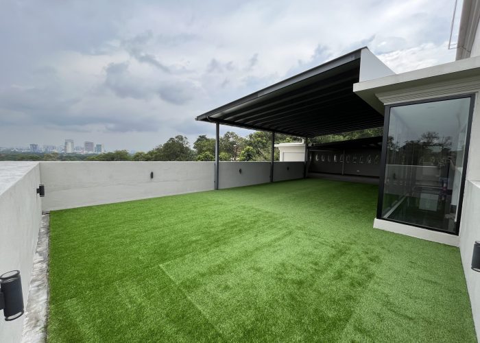 Modern backyard with artificial grass lawn, minimalist white fencing, and a covered patio area in a contemporary residential neighborhood with high-rise buildings.