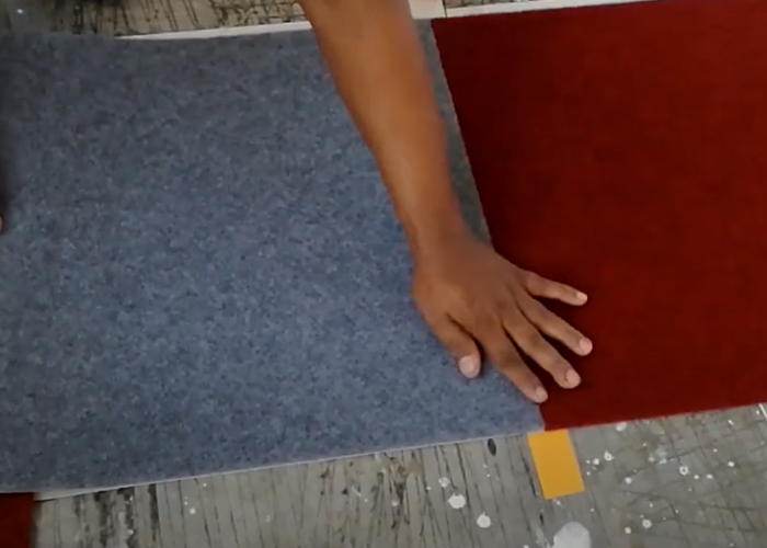 Professional Installer aligning grey and red carpet tiles during carpet tiles installation on the office floor.