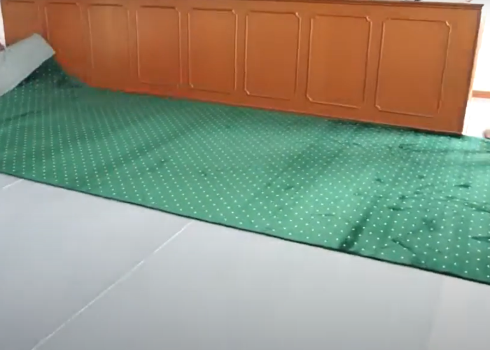 A worker opening the green carpet roll to install on the work space