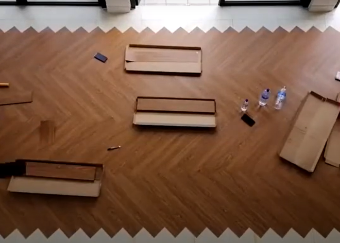Installation of chevron-patterned light brown wooden flooring, with tools and cardboard boxes.